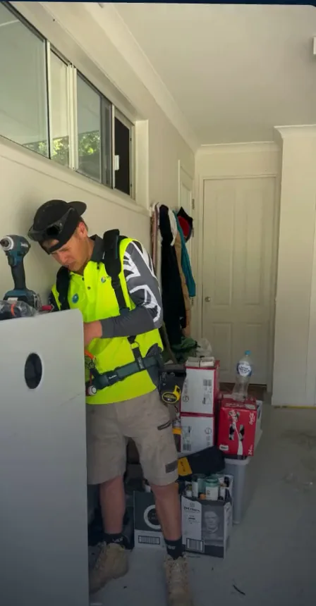An installer in high visibility clothing fitting a home battery inside a garage