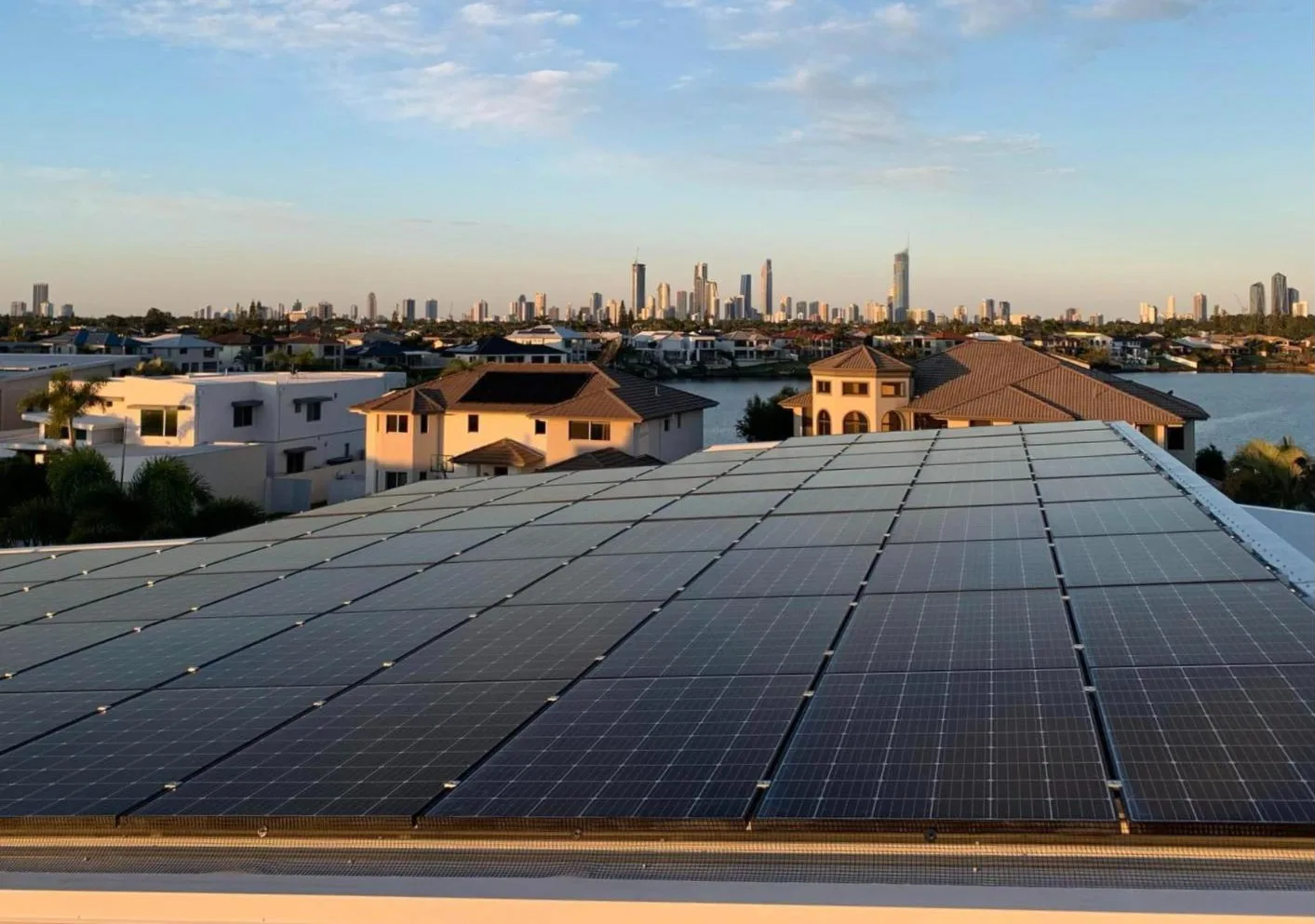 Solar panels on a rooftop at golden hour with the Gold Coast skyline behind