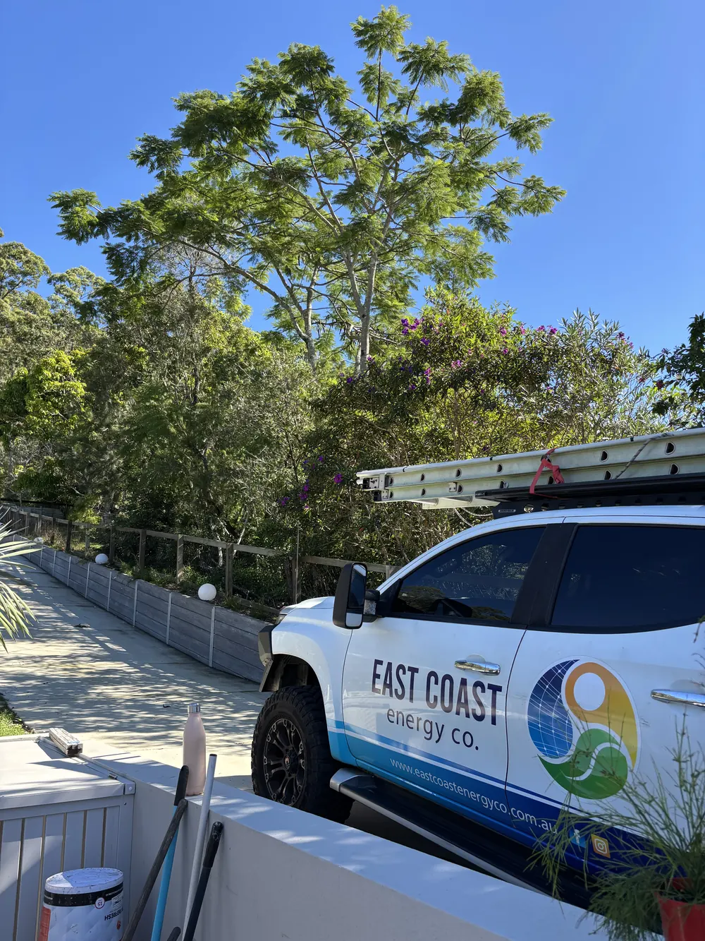 East Coast Energy branded ute with a ladder on its roof racks parked on a leafy street
